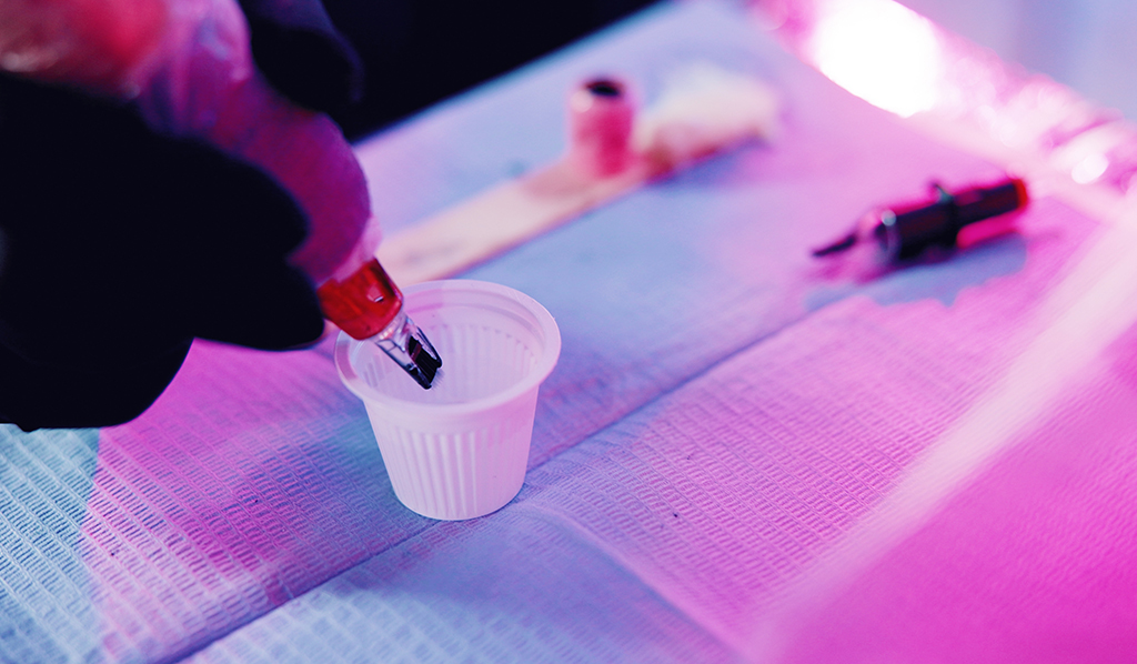 Manos, tatuador y máquina en taza de tinta para la higiene, esterilización y preparación en estudio.